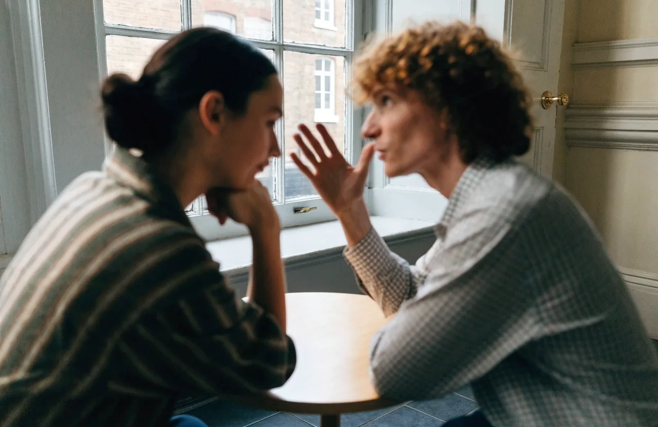 Adult learner in conversation with a tutor across a small round table in a London classroom