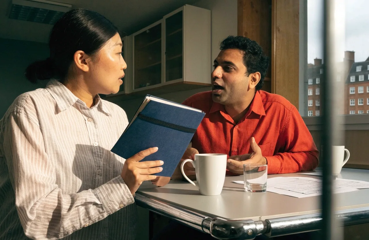 Two tutors reviewing a closed lesson plan together at a corner table in a London language school